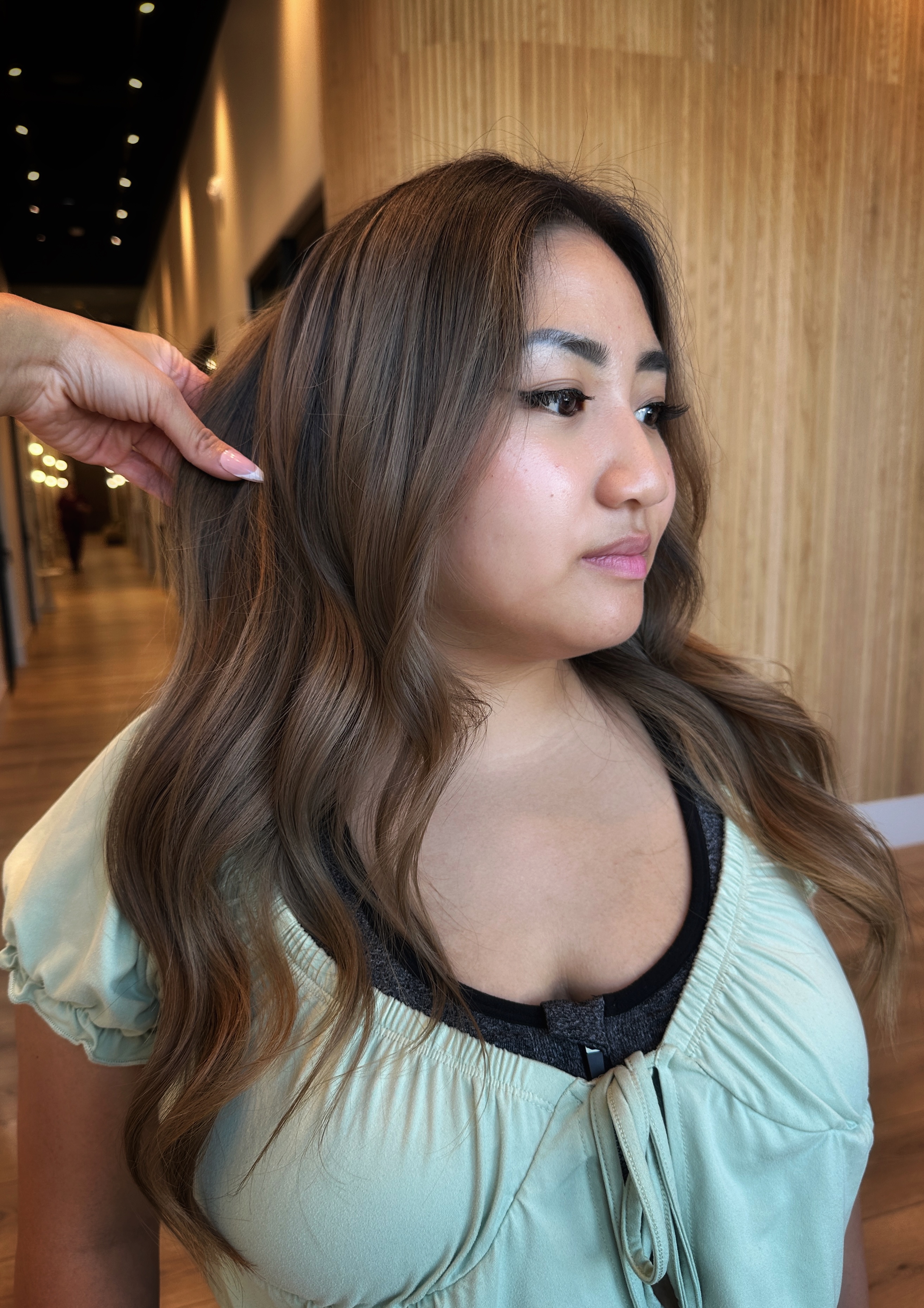 Warm caramel balayage on long wavy brunette hair, soft beach waves finish — vegan hair color near Rancho Cucamonga at Likha Studio, Fontana CA